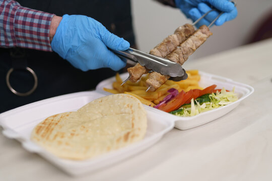 Chef put grilled meat into a lunch box with traditional Greek kalamaki dish. The cook takes pork fillet with tongs