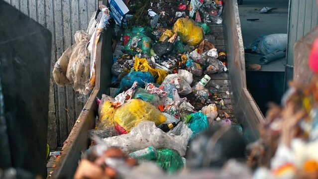 Workers loading garbage onto a conveyor belt at waste sorting plant. Slow motion