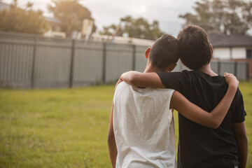 Two aboriginal boys with their arms around one another looking away