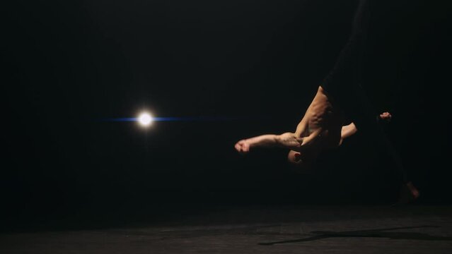A male athlete is performing acrobatics in gym. Gymnast is jumping and doing flips. Concept of exercises or acrobatic elements and training. Slow motion.
