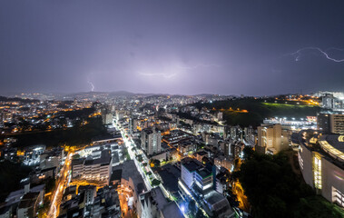 Naklejka premium Lightning storm striking skyscrapers in urban skyline at night