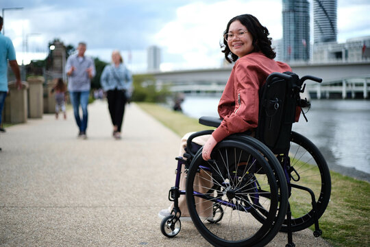 Smiling woman in wheelchair by river with city in background