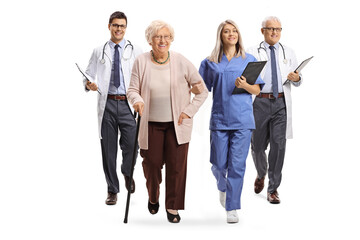 Full length portrait of a young female nurse and male doctors walking with an elderly female patient - obrazy, fototapety, plakaty