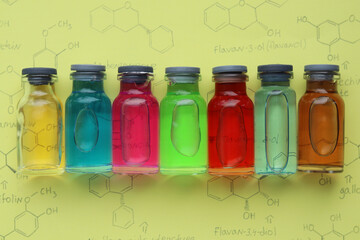Colored organic dyes in small glass bottles on a yellow background with graphic images of organic molecules.
