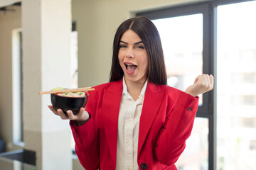 pretty young woman feeling shocked,laughing and celebrating success. japanese ramen bowl concept