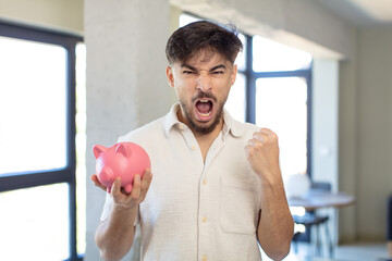 young handsome man looking angry, annoyed and frustrated. piggy bank concept