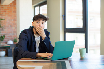 young handsome man covering mouth with a hand and shocked or surprised expression. freelance concept with laptop