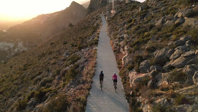 Sunset Ride.Two cyclists enjoying a scenic route along an empty mountain road in Spain with stunning views of the sunnset and mountains. Aerial drone video, follow shot. Alicante, Costa Blanca, Calpe