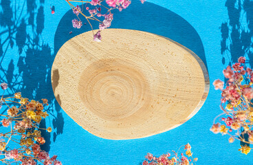 Wooden podium made of natural wood with small flowers on a blue background with shadows. View from above.Presentation of eco-products, layout