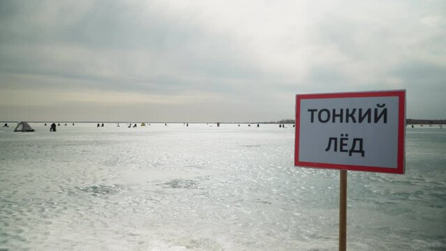 "Thin Ice" sign warning people not to go out on the ice. Sign on the background of fishermen fishing on the ice. Stop, danger, warning.	