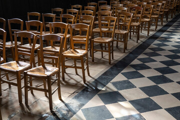 Fototapeta na wymiar Wooden chairs in the aisle of church interior with patterned flooring, France