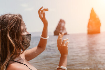 Woman summer travel sea. Happy tourist in black mask enjoy taking picture outdoors for memories. Woman traveler posing on the beach at sea surrounded by volcanic mountains, sharing travel adventure