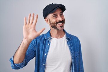 Hispanic man with beard standing over isolated background waiving saying hello happy and smiling, friendly welcome gesture