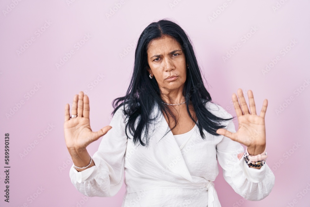 Poster Mature hispanic woman standing over pink background moving away hands palms showing refusal and denial with afraid and disgusting expression. stop and forbidden.