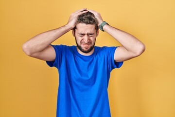 Fototapeta na wymiar Hispanic man with beard standing over yellow background suffering from headache desperate and stressed because pain and migraine. hands on head.