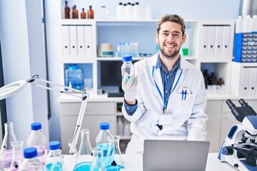 Young man scientist using laptop holding bottle at laboratory