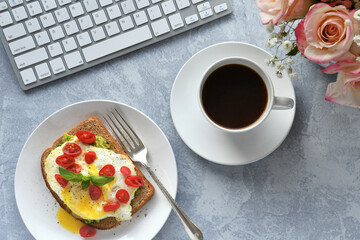 Avocado toast with fried egg on desk with computer keyboard & coffee. Eating at work desk