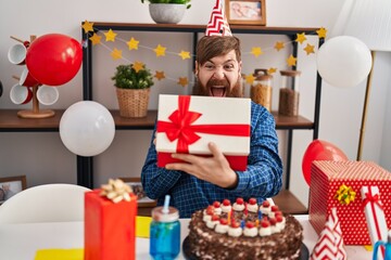 Young redhead man celebrating birthday unpacking gift at home