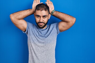 Middle east man with beard standing over blue background doing bunny ears gesture with hands palms looking cynical and skeptical. easter rabbit concept.