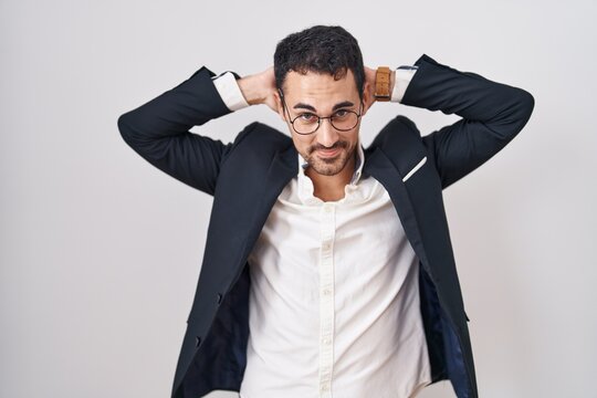 Handsome business hispanic man standing over white background relaxing and stretching, arms and hands behind head and neck smiling happy