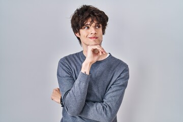 Young man standing over isolated background with hand on chin thinking about question, pensive expression. smiling and thoughtful face. doubt concept.