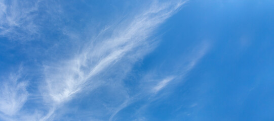 Natural white cirrus clouds as feathers are diagonally on blue sky. Skyscape. Banner. Copy space.