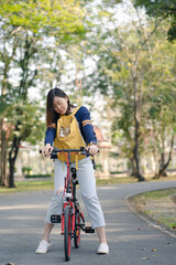 Fototapeta premium asian woman biking bicycle with her cat in backpack at park