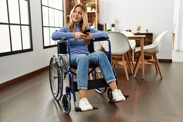 Young caucasian woman using smartphone sitting on wheelchair at home