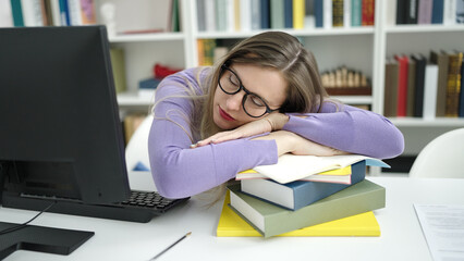 Young blonde woman student writing on notebook with head on table at library university