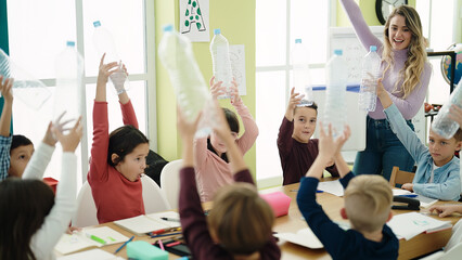Woman and group of kids having recycling lesson holding empty bottle at classroom