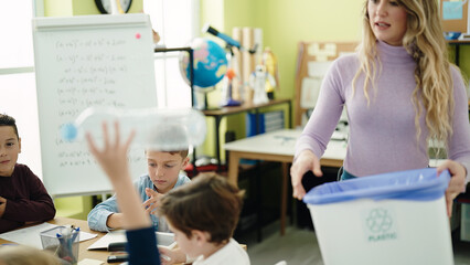 Woman and group of kids throwing plastic bottle on paper bin recycling at classroom