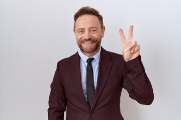 Middle age business man with beard wearing suit and tie showing and pointing up with fingers number two while smiling confident and happy.
