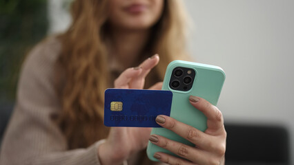 Young beautiful hispanic woman using smartphone and credit card sitting on sofa at home