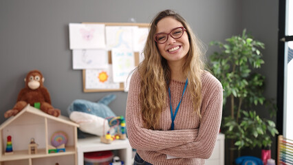 Young beautiful hispanic woman preschool teacher smiling confident standing with arms crossed...