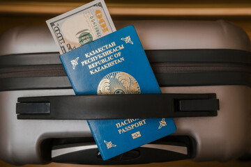 The passport of Republic of Kazakhstan lies on the grey suitcase. Soft focus. Dollar currency is sticking out of the passport.