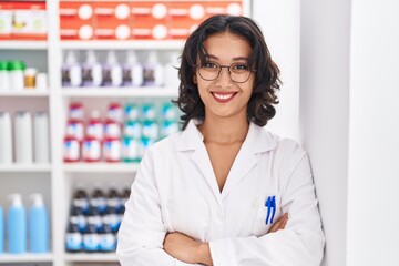 Young beautiful hispanic woman pharmacist smiling confident standing with arms crossed gesture at...