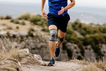 male runner with knee pads running on mountain trail, protective compression sleeves against...