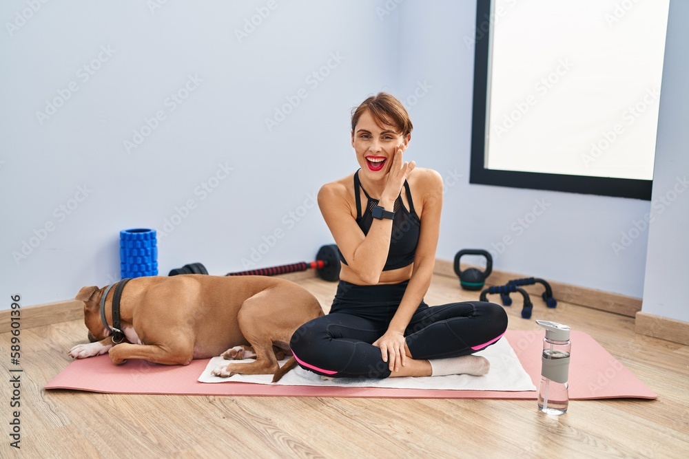 Sticker young beautiful woman sitting on yoga mat hand on mouth telling secret rumor, whispering malicious t