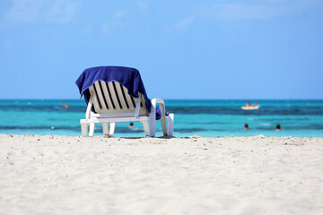 Deck chair with blue towel on sandy beach on swimming people background. Sea resort on Caribbean...