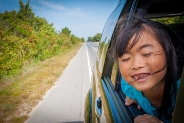 Young asian girl enjoying the breeze while on a drive with the window open