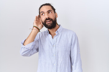 Hispanic man with beard wearing casual shirt smiling with hand over ear listening an hearing to rumor or gossip. deafness concept.