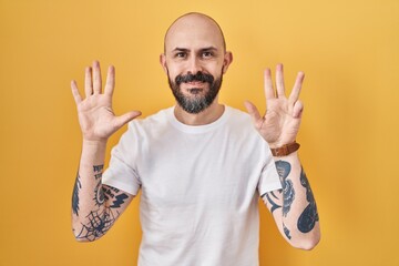 Young hispanic man with tattoos standing over yellow background showing and pointing up with...