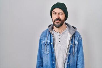 Young hispanic man with tattoos wearing wool cap winking looking at the camera with sexy expression, cheerful and happy face.