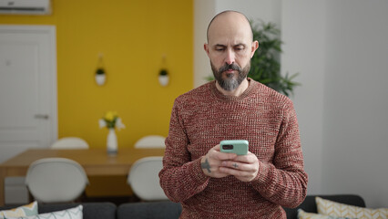 Young bald man using smartphone standing at home