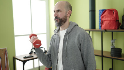 Fototapeta premium Young bald man smiling confident using dumbbell training at sport center