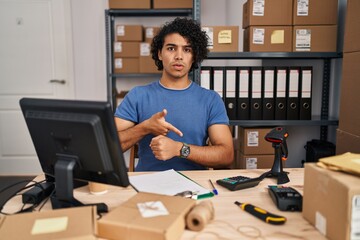 Hispanic man with curly hair working at small business ecommerce in hurry pointing to watch time, impatience, upset and angry for deadline delay