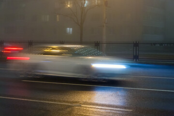 Blurred car movement down the street on a foggy evening.