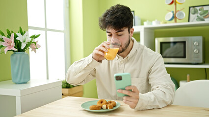 Fototapeta na wymiar Young hispanic man having breakfast using smartphone at dinning room