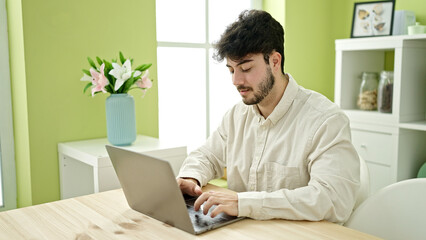 Young hispanic man using laptop sitting on table at dinning room
