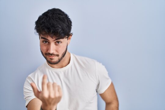 Hispanic man with beard standing over white background beckoning come here gesture with hand inviting welcoming happy and smiling